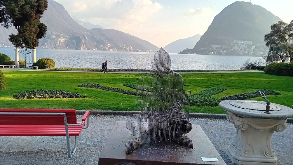 A sculpture in a park with a lake and mountains in the background. 1