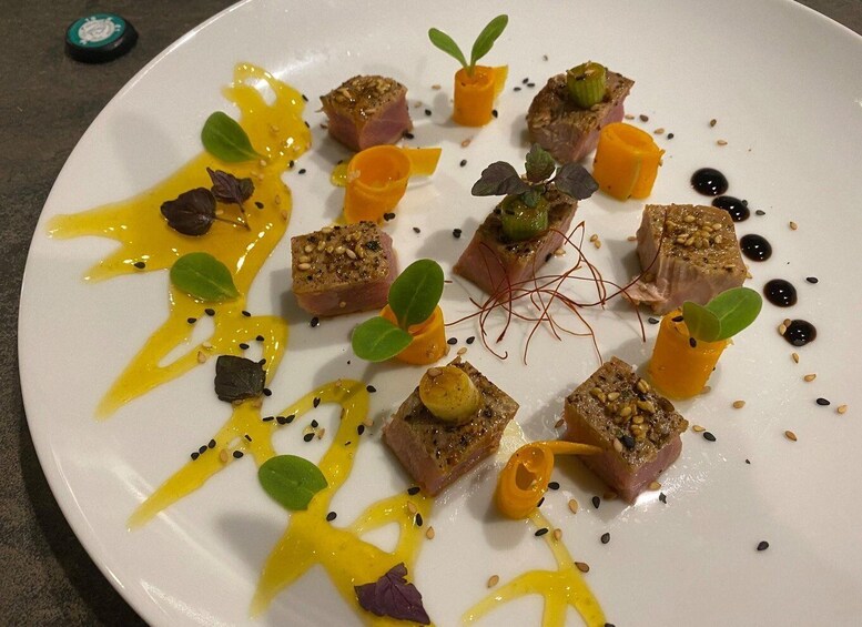 A white plate with food arranged in a circular pattern, garnished with green leaves, orange cubes, and black seeds. 2