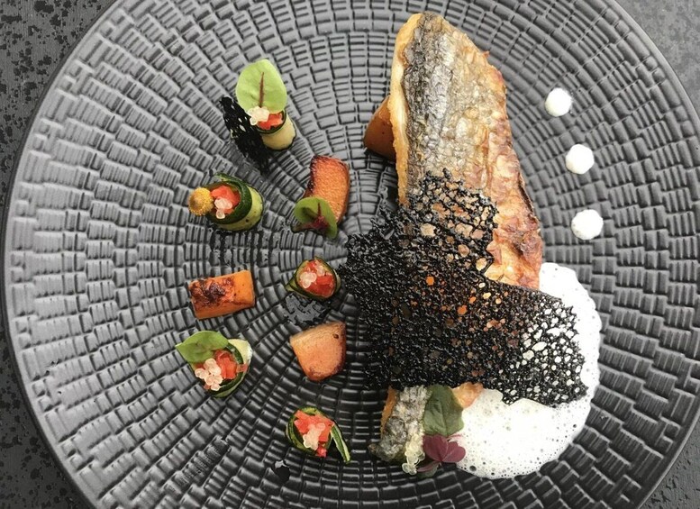A plate with a piece of fish, vegetables, and a decorative element. 1