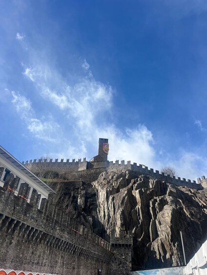 A historic stone fortress with a prominent tower, steep rocky walls, and a clear blue sky. 5