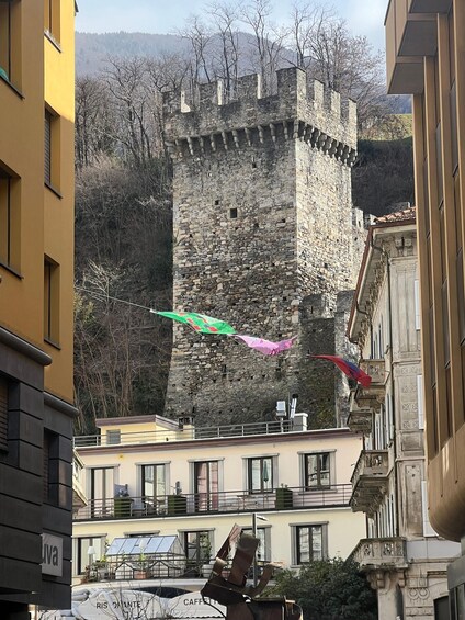 A stone tower with flags, modern buildings, and a mountain backdrop. 3
