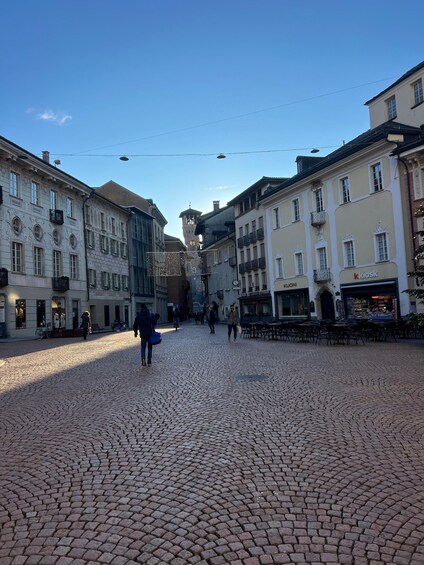 A cobblestone square with historic buildings, a clock tower, and a kiosk. 2