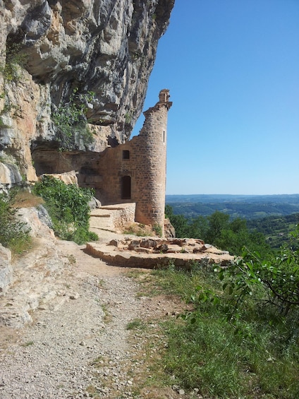 A stone ruin with a tower, surrounded by rocky cliffs and greenery. 4
