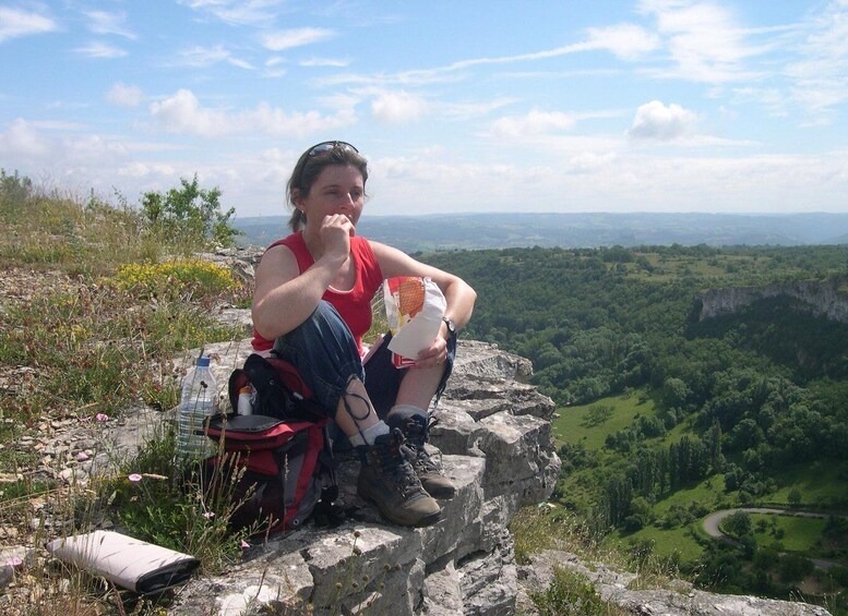 A person sitting on a rock with a backpack and a bottle, overlooking a valley. 2