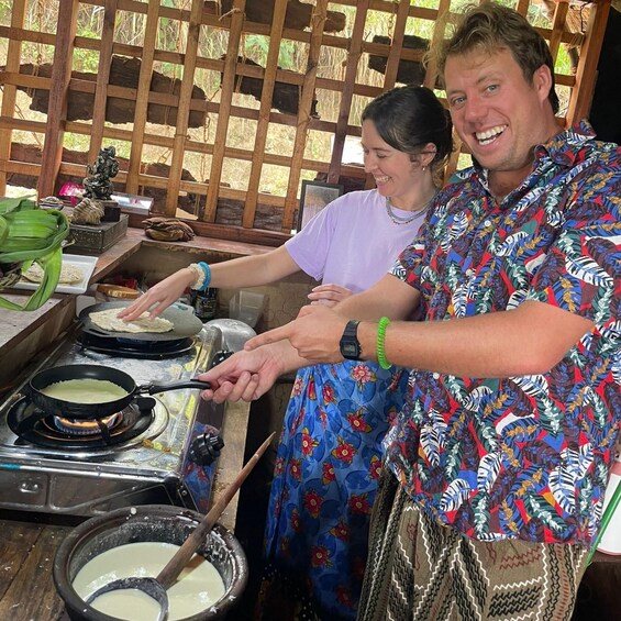 Two people cooking tortillas on a stove, with a pot of sauce nearby. 4