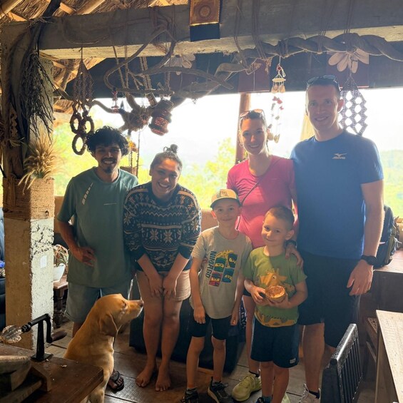 A group of people and a dog indoors with rustic decor and a thatched roof. 3