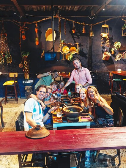 A group of people dining at a rustic restaurant with a wooden table and hanging decorations. 1