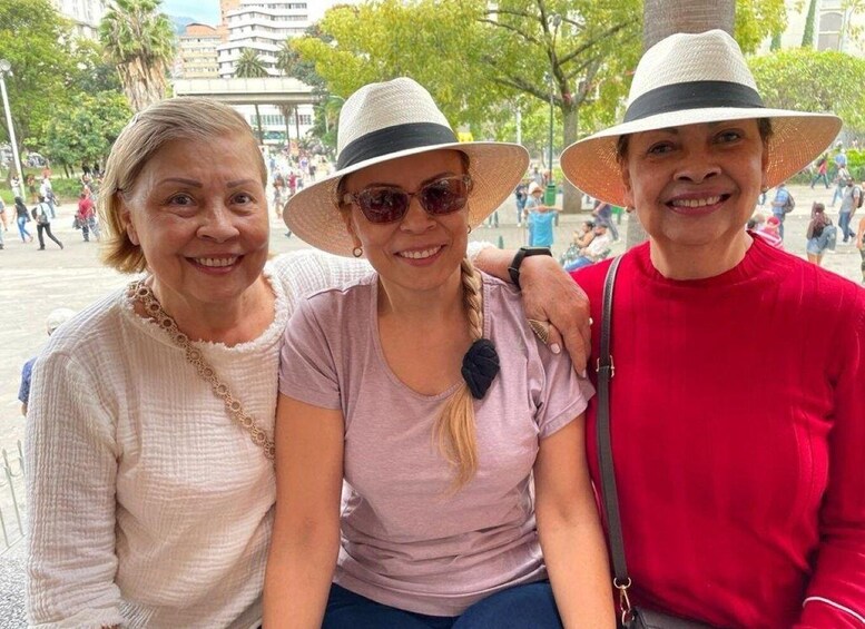 Three people sitting on a bench in a public square with trees and buildings in the background. 5