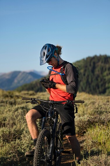 A person sitting on a mountain bike in a grassy field with mountains in the background. 1