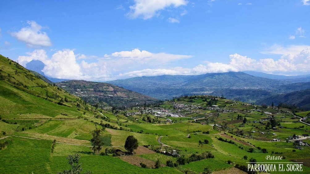 A valley with green fields, a small town, and distant mountains under a clear sky. 2