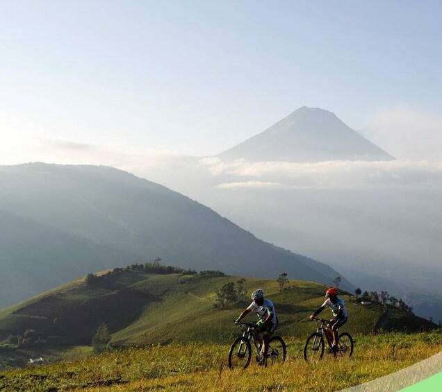 Two cyclists on a grassy hill with a mountain in the background. 3