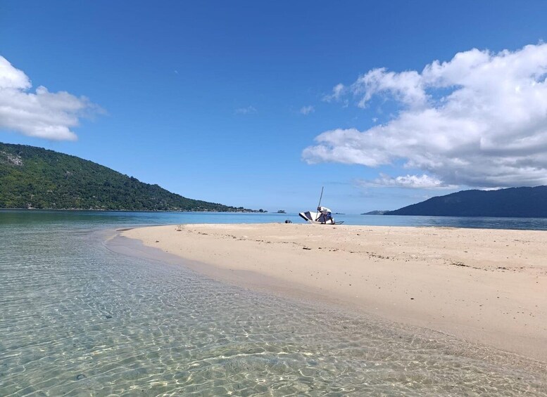 A beach with clear shallow waters, a person in a boat, and distant mountains. 4