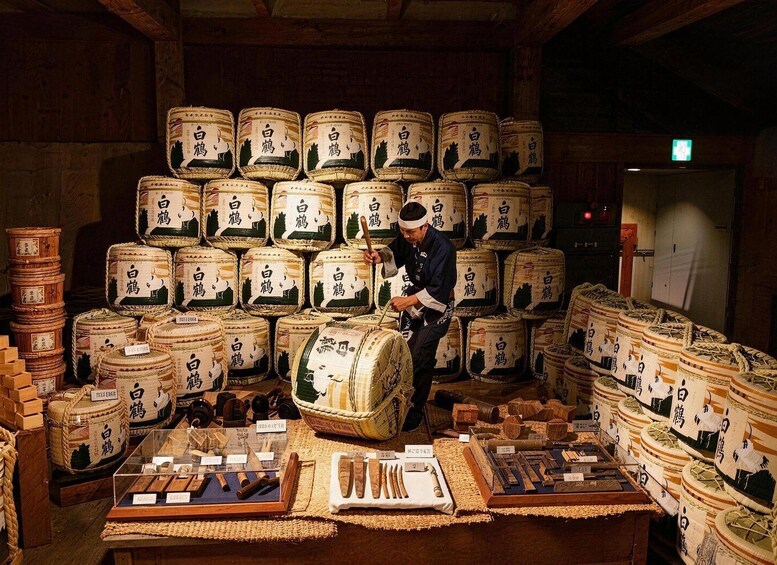 A person in a uniform surrounded by large, traditional Japanese sake barrels. 1