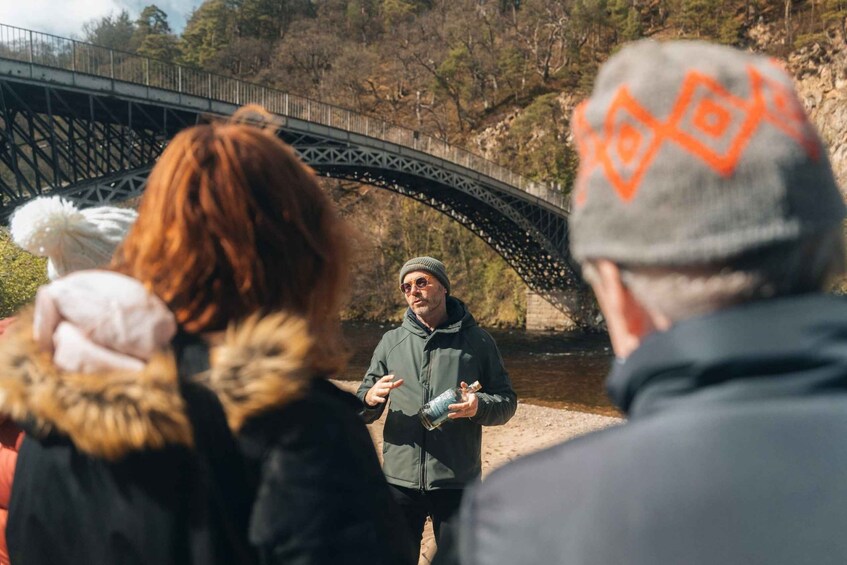 A group of people standing near a bridge with a river and trees in the background. 1