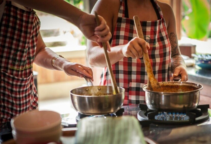 Two people cooking, one stirring a pot on a stove and the other holding a ladle. 4