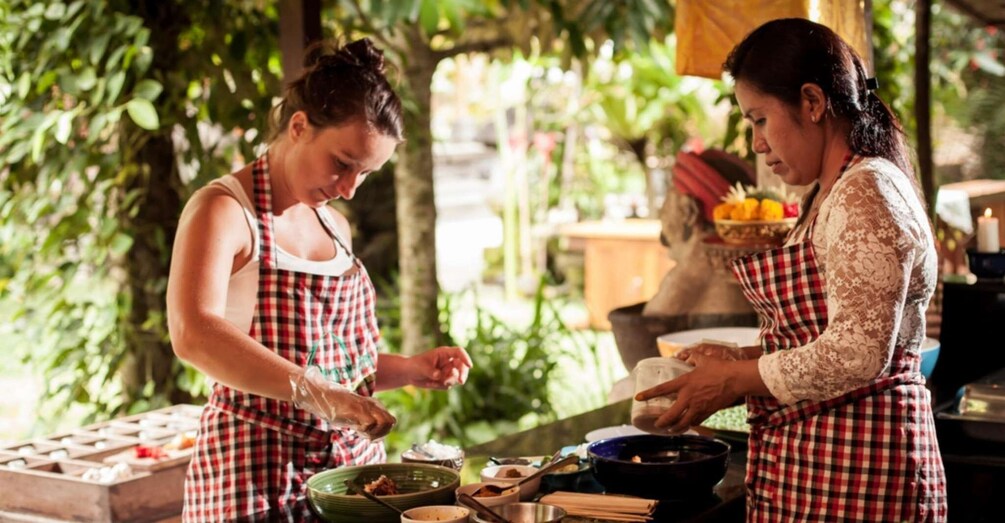 Two people cooking outdoors with a variety of ingredients and cooking utensils on the table. 2