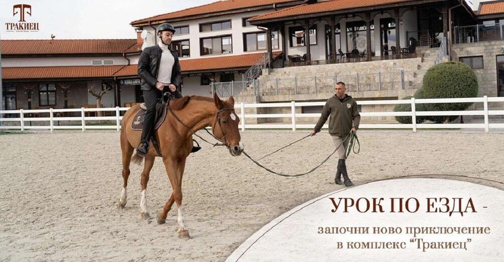 A horse training session in an indoor arena with a white fence and a building in the background. 5