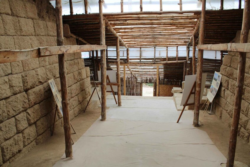 A rustic interior with exposed wooden beams, a brick wall, and easels with blank canvases. 2