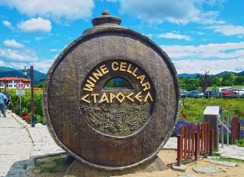 A large wooden barrel with 'WINE CELLAR' engraved on it, surrounded by a garden with flowers and a clear sky. 4
