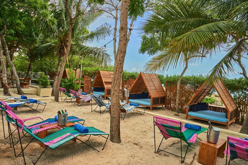 A beach with colorful lounge chairs, wooden cabanas, and palm trees. 2