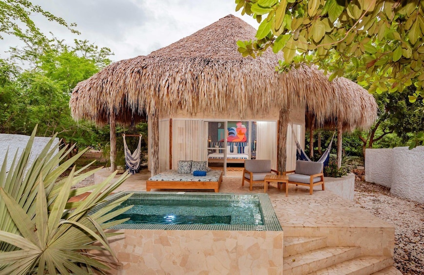 A thatched-roof hut with a pool, surrounded by greenery. 1