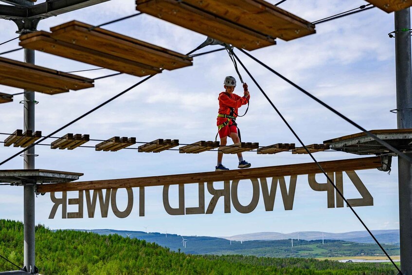 A person on a suspended bridge with the words 'ZIRKWOOD TOWER' visible. 1