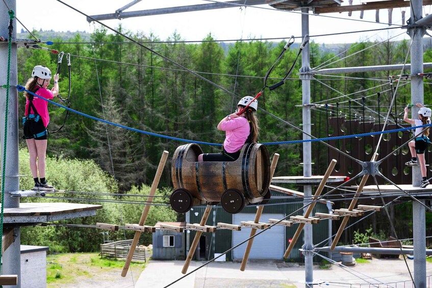 An outdoor adventure course with a wooden barrel ride, ropes, and a forested backdrop. 3