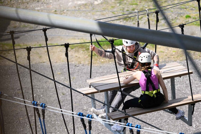 A person on a rope bridge with another person assisting. 4