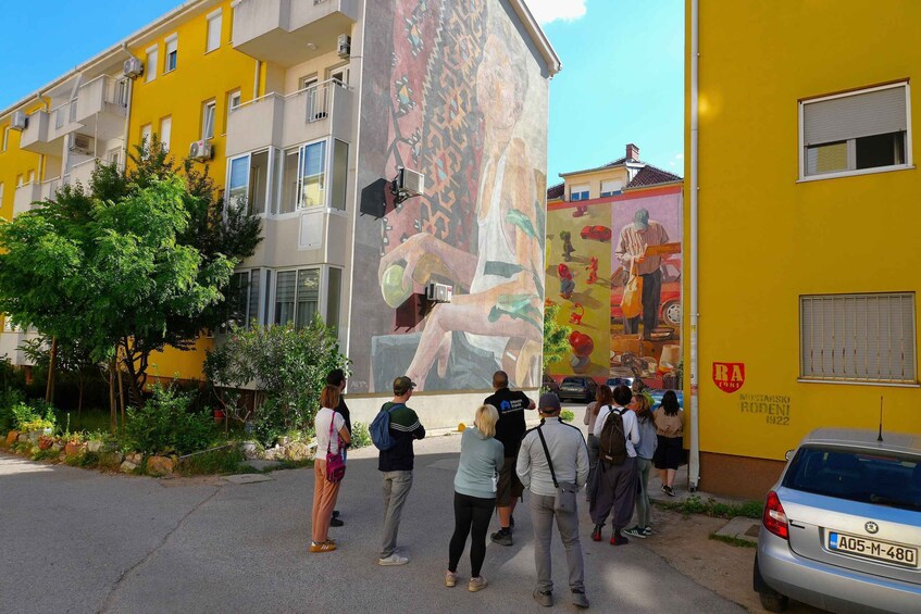A mural on a yellow building with people observing it. 2
