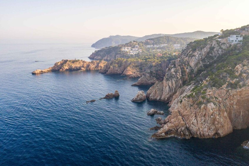 A coastal landscape with rocky cliffs, calm sea, and scattered buildings. 2