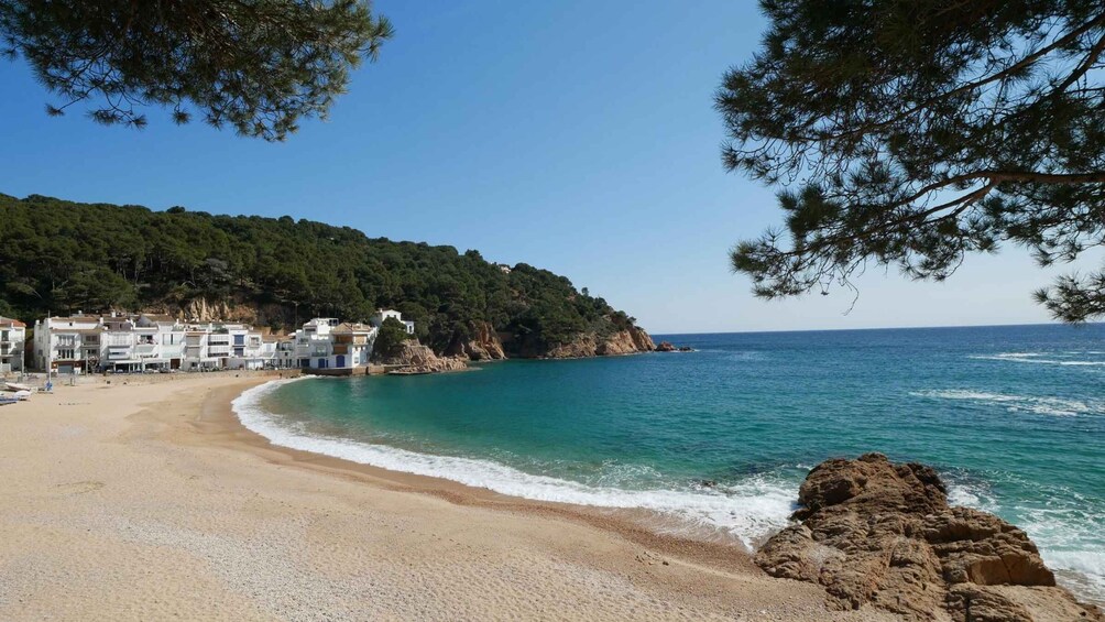 A coastal beach with clear turquoise waters, a sandy shore, and buildings on a hillside. 4
