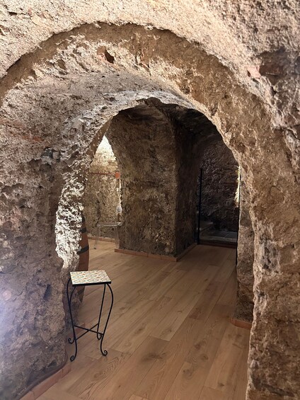 An interior space with a wooden floor, a table, and a chair, framed by a stone archway. 3