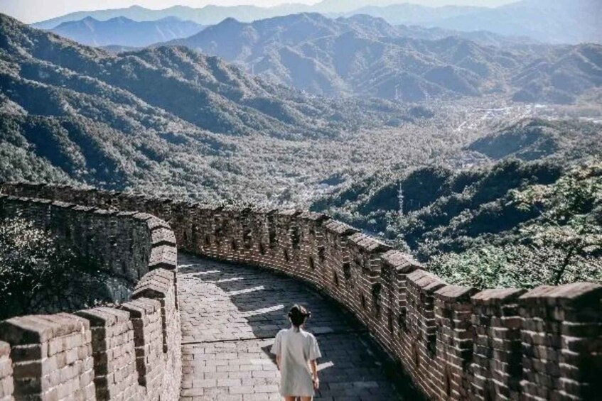 A person walking along the Great Wall of China, surrounded by mountainous terrain. 4