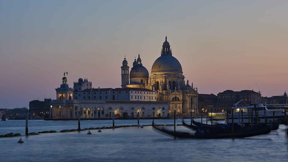 A grand historical building with multiple domes and towers, a body of water with gondolas, and a sunset sky. 3