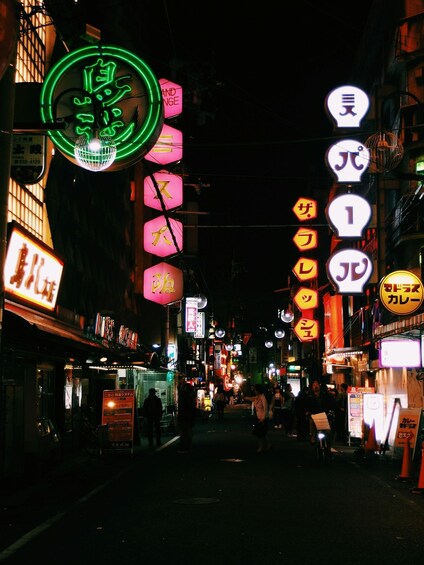 A neon-lit street at night with signs in various colors and languages. 3