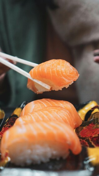 A close-up of a person holding a piece of salmon sushi with chopsticks. 4