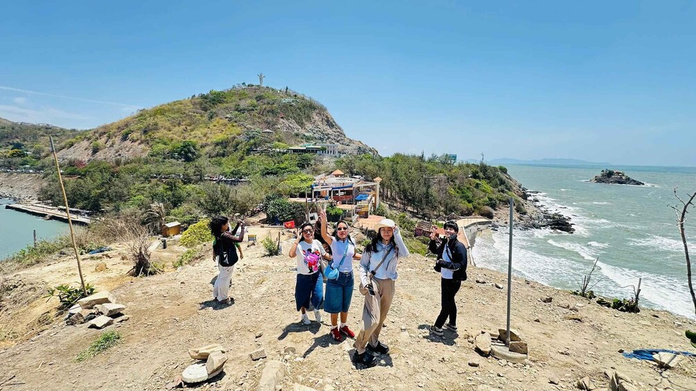 A group of people on a rocky hillside overlooking a coastal area with a hilltop monument and a small island in the water. 2