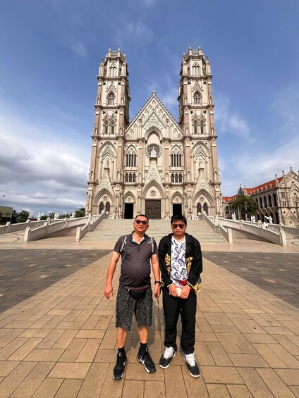 Two people standing in front of a large, ornate cathedral with twin towers and a central rose window. 4