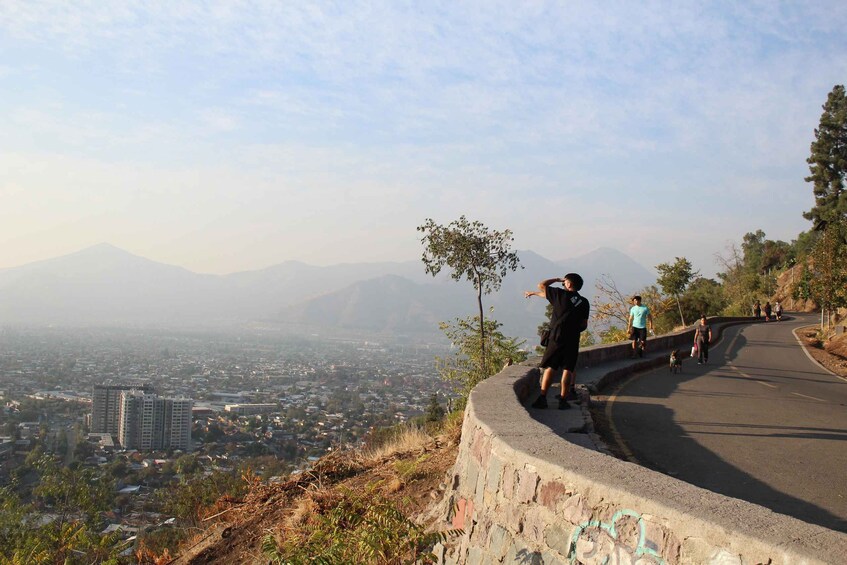 A curved road with people walking, a cityscape in the background, and mountains. 1