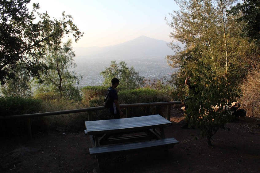 A person standing at a wooden bench overlooking a mountain. 4