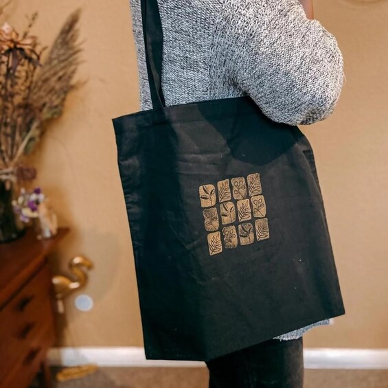 A person holding a black tote bag with a gold pattern. 4