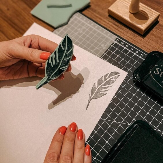 A hand holding a leaf-shaped paper cutout, a ruler, and a cutting mat on a table. 1
