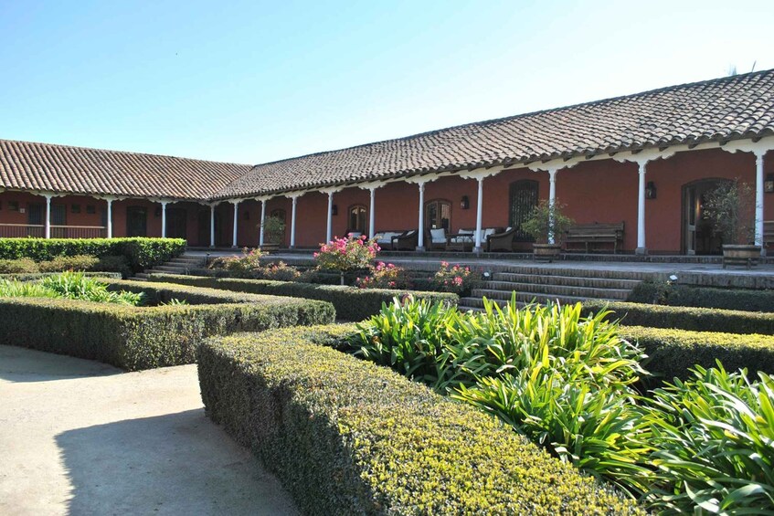 A courtyard with a tiled-roof building, neatly trimmed hedges, and a bench. 2