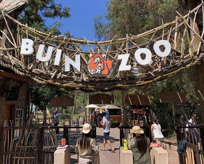 A sign for the Bunjil Zoo with a tiger graphic, surrounded by trees and visitors. 1