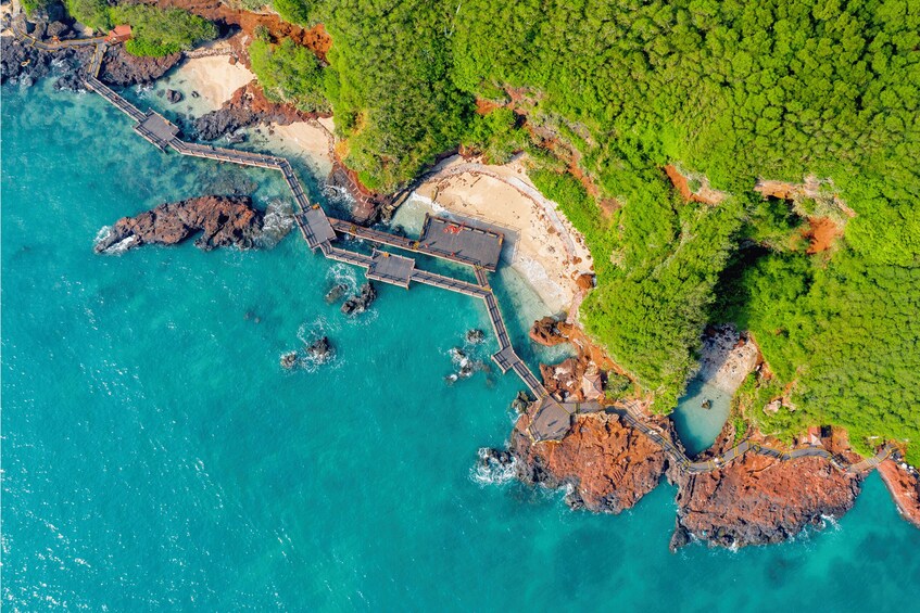 An aerial view of a coastal area with a pier extending into turquoise waters, surrounded by lush greenery and rocky outcrops. 1