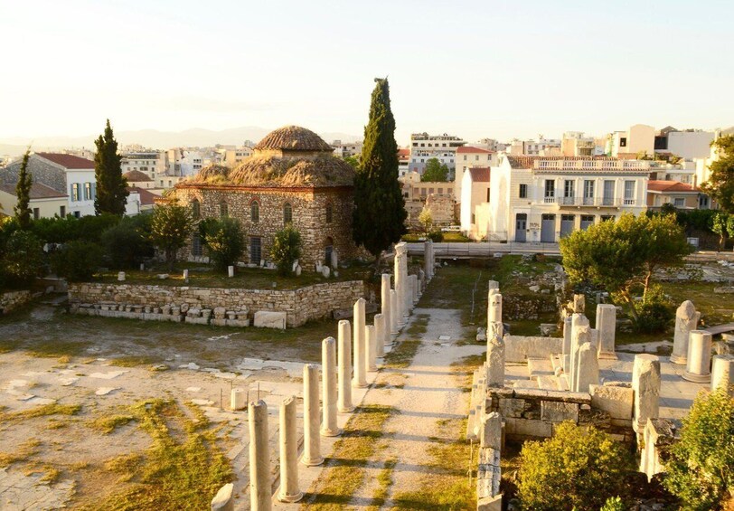 An ancient ruin with columns and a dome, surrounded by modern buildings and a clear sky. 2