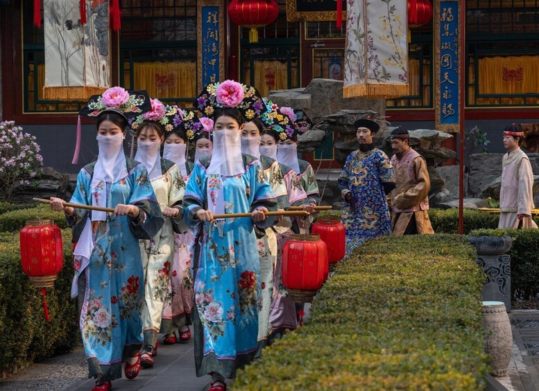 A group of people in traditional attire walking with staffs, in front of a building with Chinese characters and red lanterns. 4