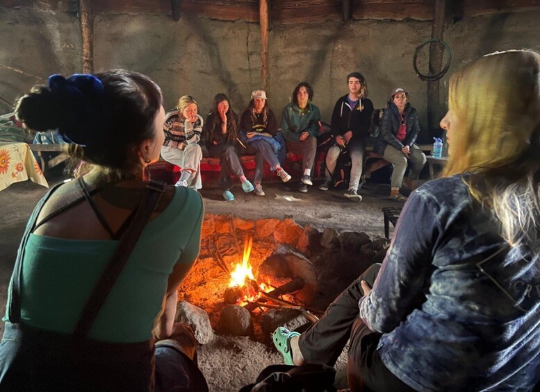 A group of people sitting around a campfire in a rustic setting. 1