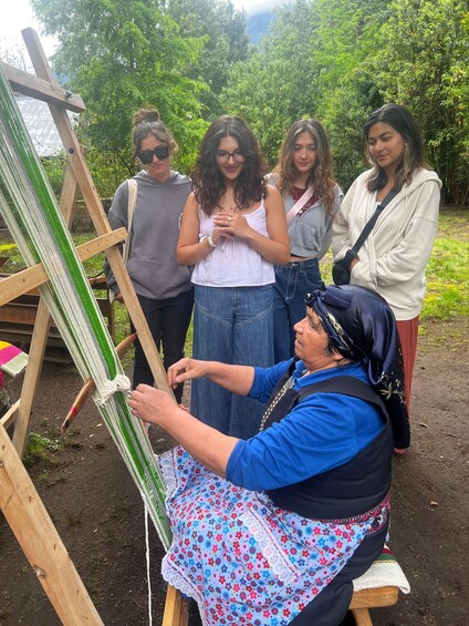 A person weaving on a loom outdoors with a group of onlookers. 2