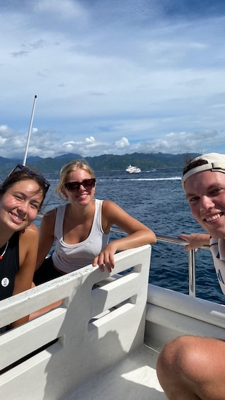 Three people on a boat with a mountainous landscape and a ship in the distance. 3